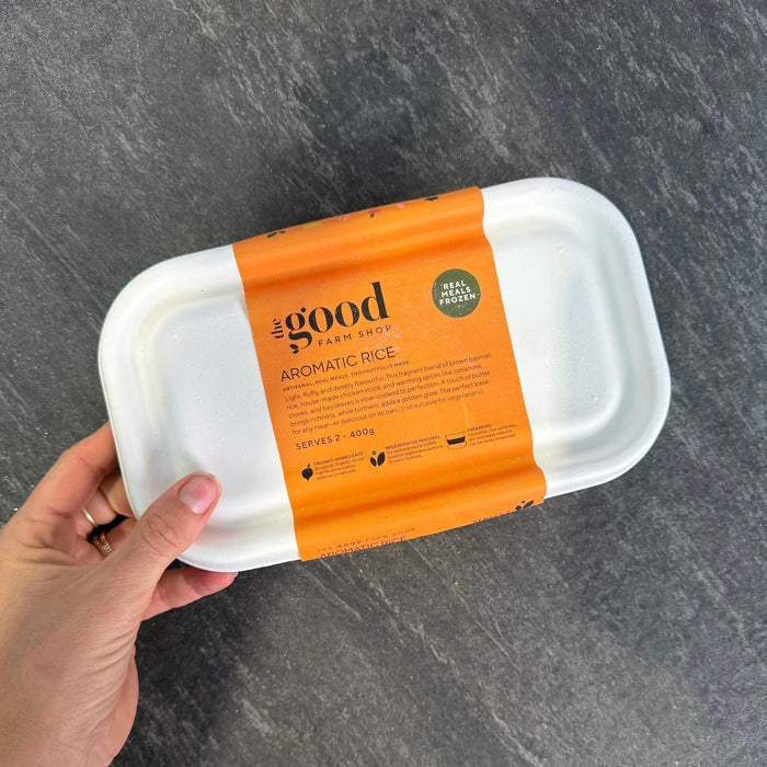 Aromatic Rice frozen meal in white container with orange label, held in hand over dark surface