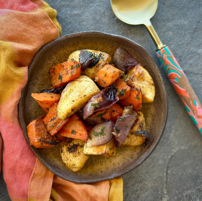 A plate of roasted vegetables including carrots, sweet potato, potato, and red onion, garnished with herbs and spices.